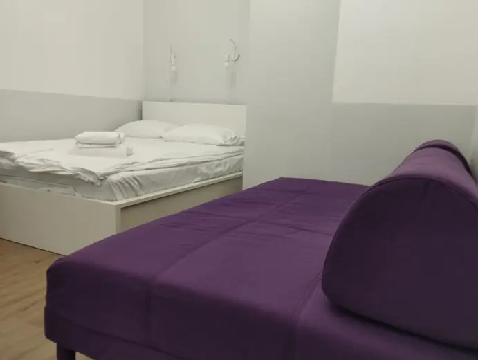 Sypialnia z białym łóżkiem i fioletowymi akcentami.