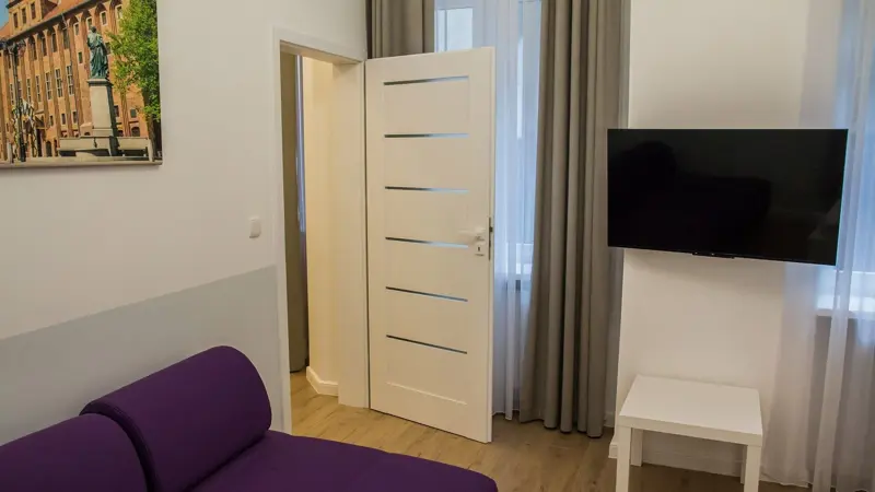 Kącik wypoczynkowy z fioletową sofą i jasnymi ścianami.
