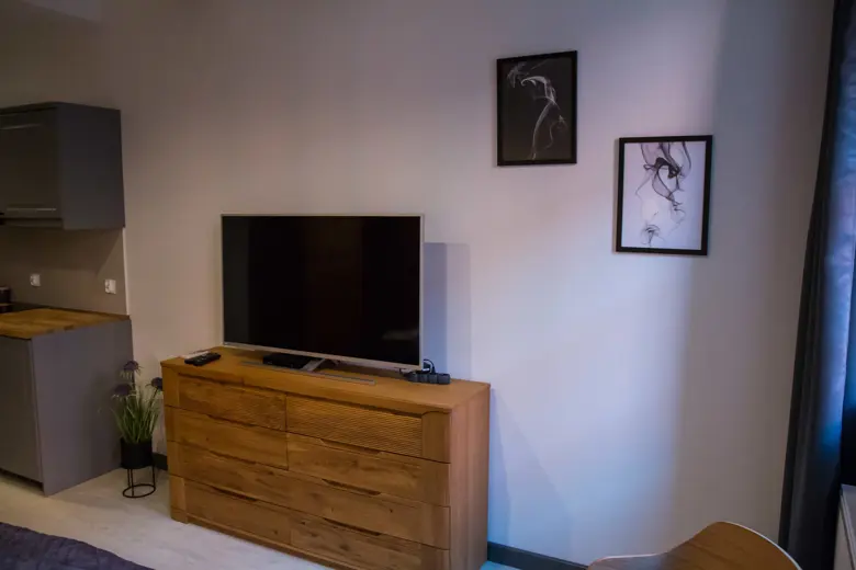 Telewizor na drewnianej komodzie w salonie, obok dekoracyjne obrazy na ścianie.