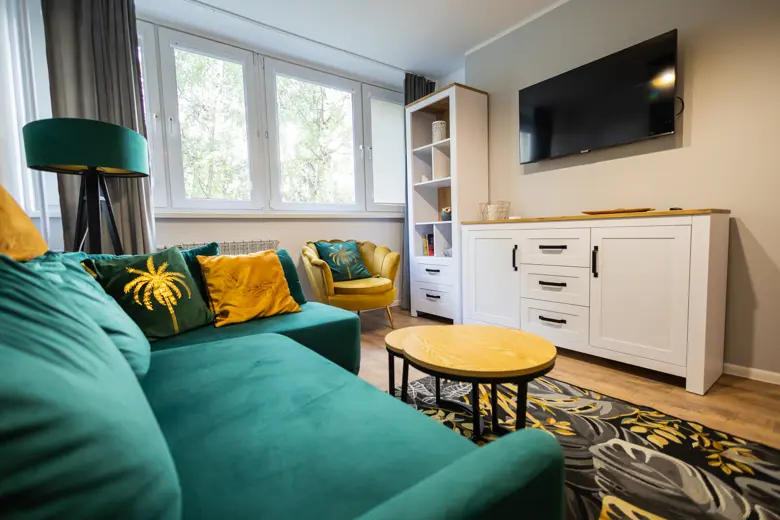 Salon z dużymi oknami, sofa w kolorze turkusowym i żółte poduszki