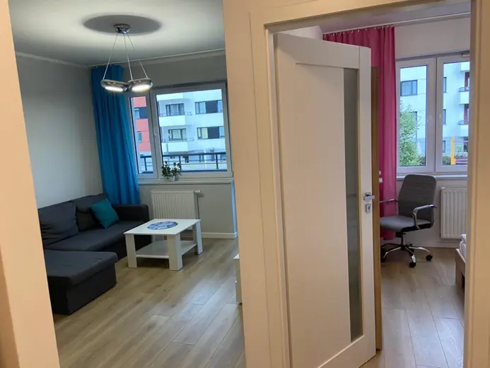 Salon z sofą w odcieniach szarości, okno z niebieskimi zasłonami