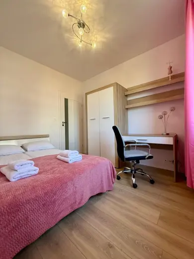 Sypialnia z różową narzutą na łóżku i świeżymi ręcznikami.