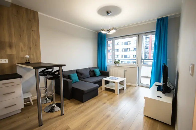 Salon z narożną sofą i dużym oknem wychodzącym na balkon.
