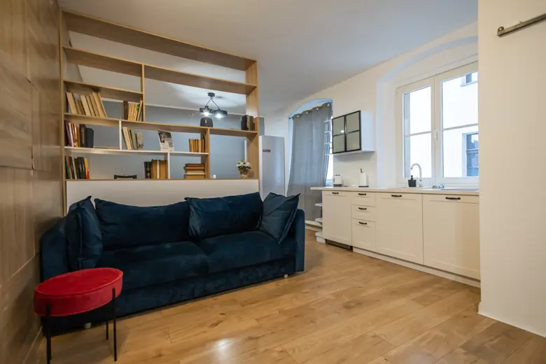 Granatowy sofa przy drewnianej półce.