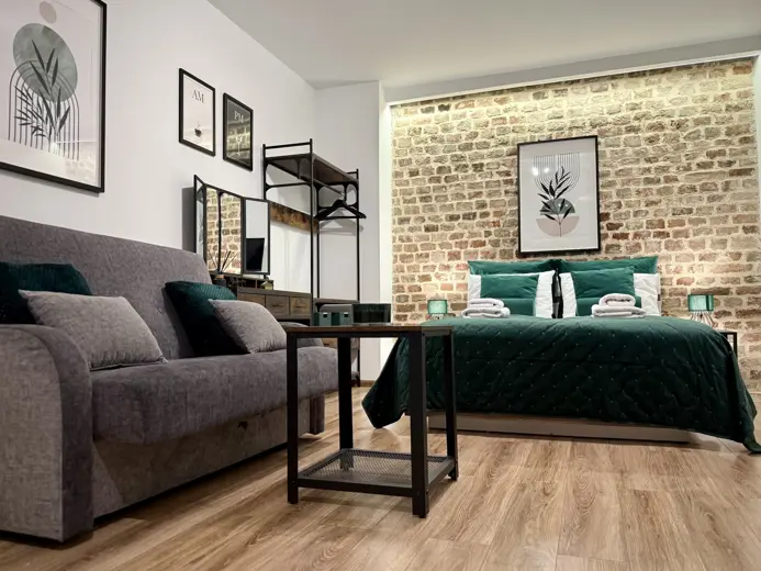 Salon z sofą szarą, drewnianą podłogą i ceglaną ścianą.
