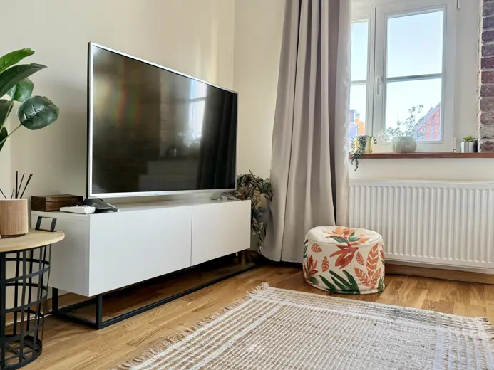 Salon z dużym telewizorem, białą szafką i jasnym dywanem.