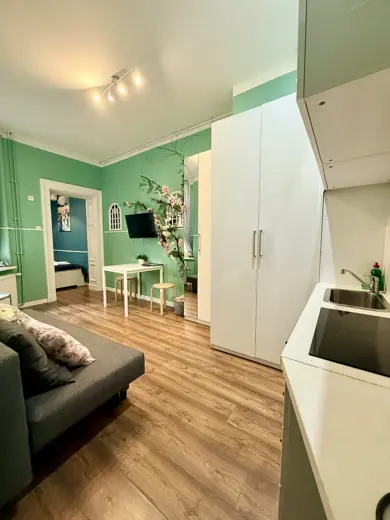 Salon z zieloną ścianą, sofą i jasnym drewnem podłogi.