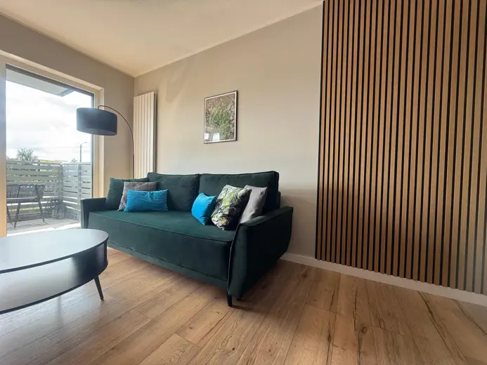 Salon z ciemnozieloną sofą i balkonem na widoku.