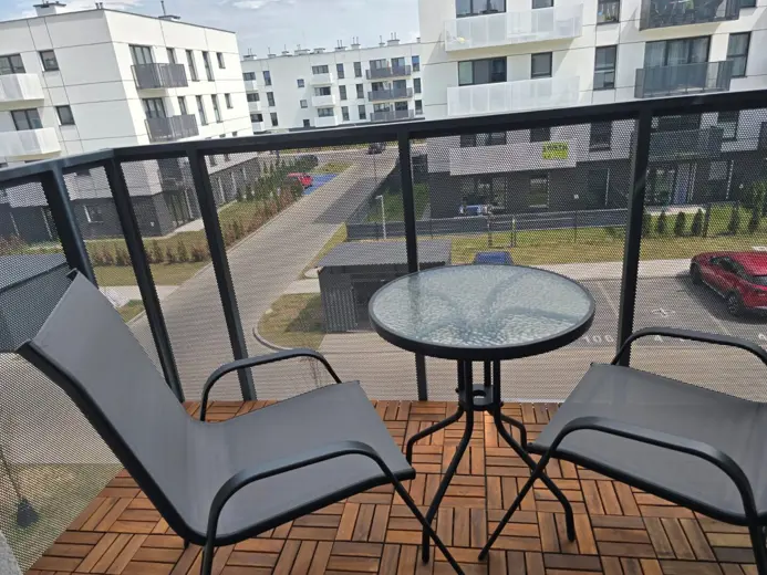Balkon z drewnianą podłogą, okrągły stolik i dwa fotele.