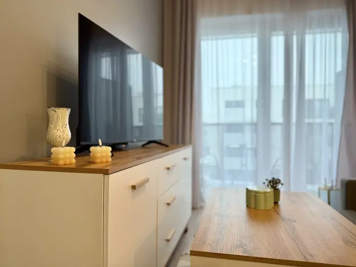 Duży telewizor na komodzie z lampkami i dekoracjami.