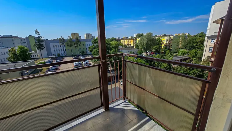 Widok z balkonu na zabudowę miejską i zieleń.