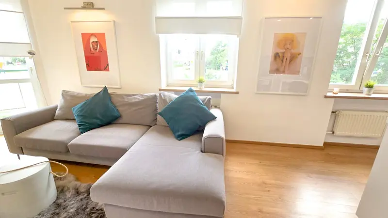 Jasny salon z sofą narożną i turkusowymi poduszkami.
