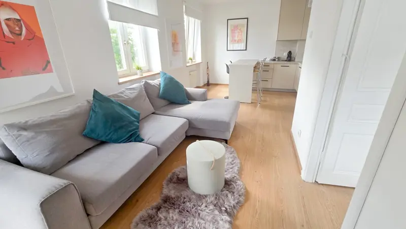 Przestronny salon z narożną sofą i widokiem na kuchnię.