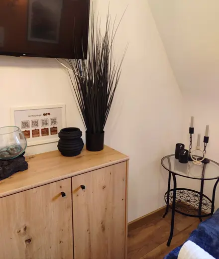 Kącik wypoczynkowy z telewizorem nad drewnianą komodą i ozdobami