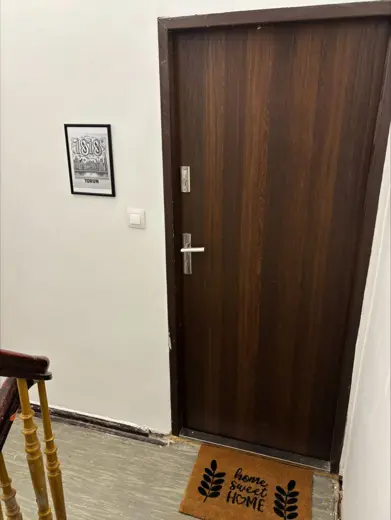 Wejście do mieszkania z ciemnymi drzwiami, mata i schody.