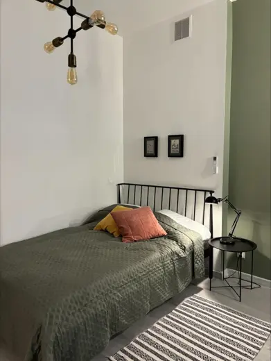 Sypialnia z czarną metalową ramą łóżka, zieloną ścianą i wiszącą lampą.