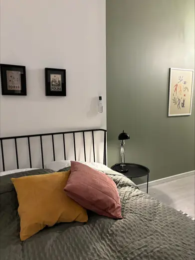 Sypialnia z czarną metalową ramą łóżka oraz zieloną ścianą, widoczna lampka nocna.