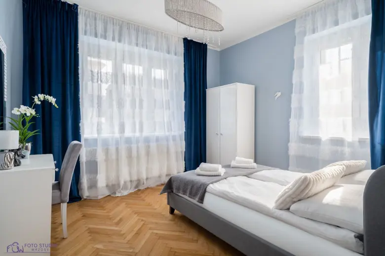 Sypialnia o błękitnych ścianach, komfortowe łóżko i zasłony