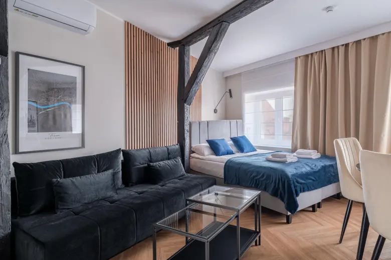 Salon z czarną sofą, elementami drewnianymi i oknem