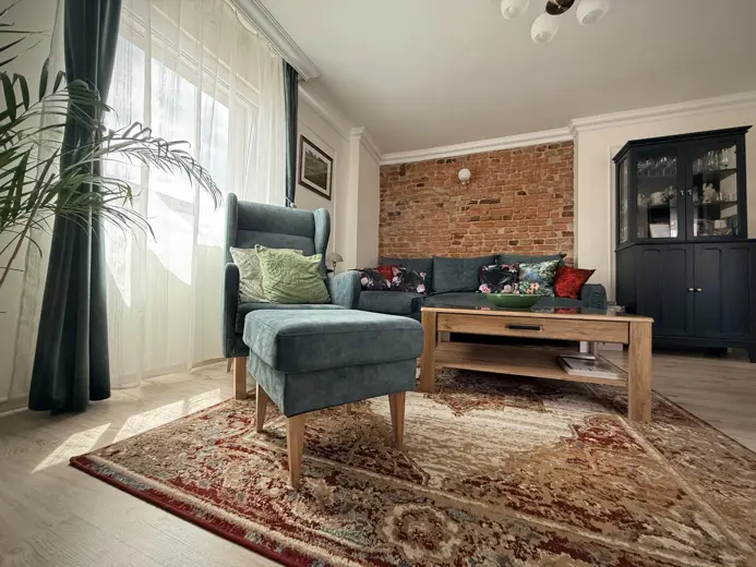 Sofa z turkusowego materiału przy ceglanej ścianie.