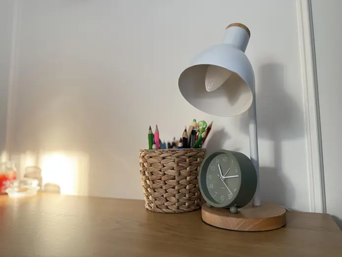 Lampka biurkowa, zegar oraz kredki w koszyku.