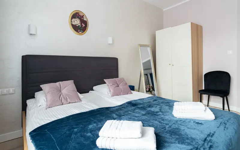 Sypialnia z dużym łóżkiem, granatową narzutą i lustrem.