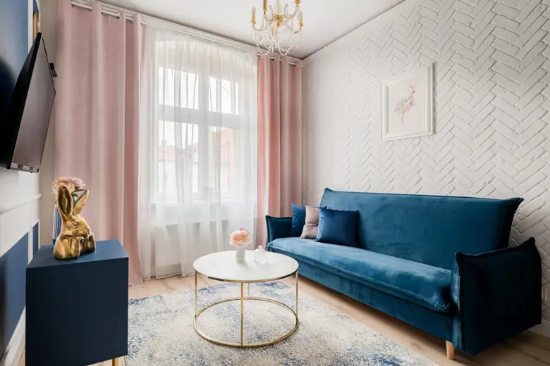 Salon z niebieską sofą, różowymi zasłonami i żyrandolem.