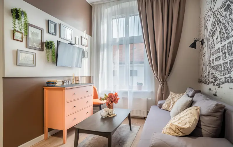 Jasny salon z obrazami na ścianie i pomarańczową komodą