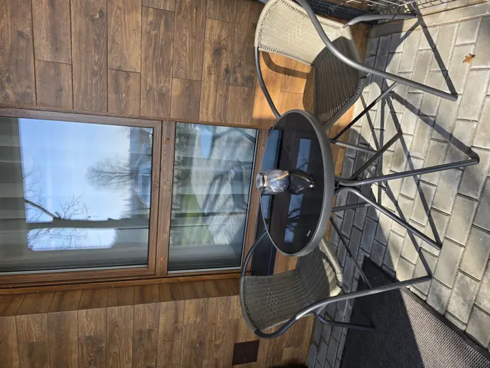 Balkon z drewnianym tarasem, okrągłym stołem i krzesłami.