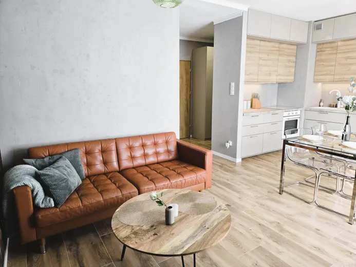 Salon z brązową skórzaną sofą i otwartą kuchnią.