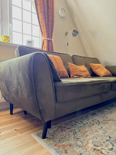 Sofa w ciemnym odcieniu z pomarańczowymi poduszkami przy oknie