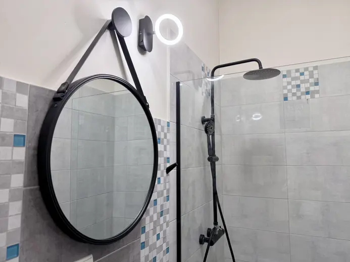 Okrągłe lustro nad parą prysznicową i lampą LED
