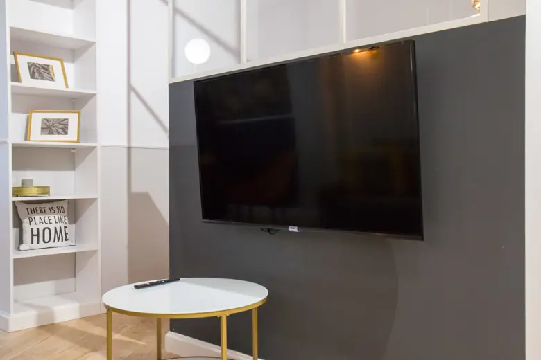 Salon z telewizorem na ciemnej ścianie i białymi półkami.