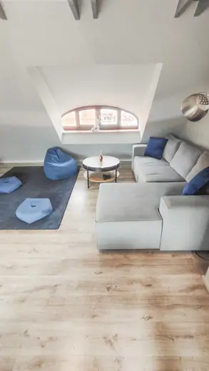 Szara sofa narożna z jasnym stolikiem i błękitnymi akcentami