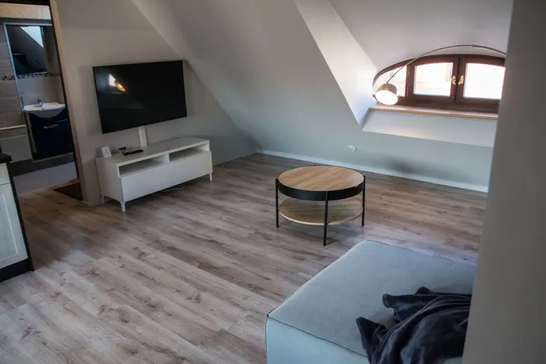 Salon z telewizorem na białej szafce i jasnym wnętrzem.