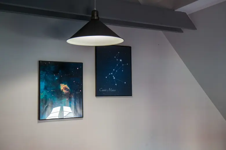 Dwa obrazy na ścianie pod wiszącym kloszem lampy.