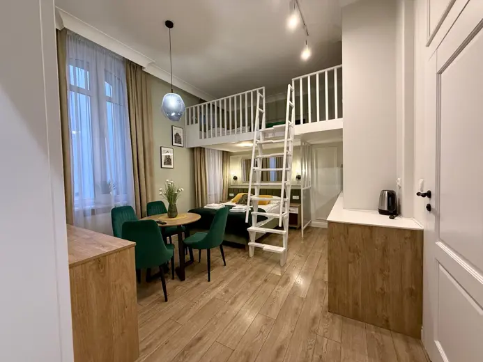 Sala z antresolą nad jadalnią i zielonymi krzesłami przy stole.