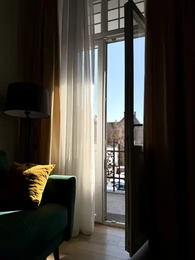 Zielona sofa przy oknie, jasne zasłony tworzące kącik.