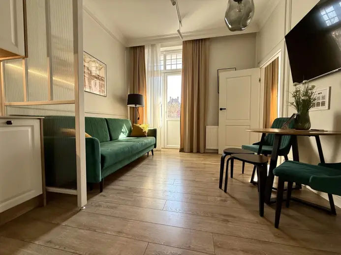 Salon z zieloną sofą, jadalnym stołem i drzwiami balkonowymi.