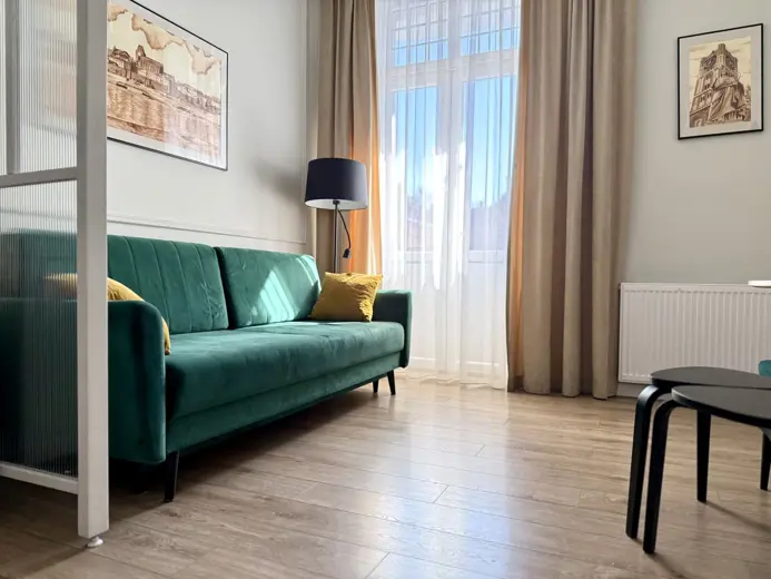 Salon z zieloną sofą, dużymi oknami i zasłonami.