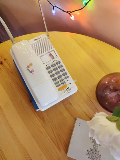 Stacjonarny telefon na okrągłym drewnianym stole, kolorowe światełka w tle.