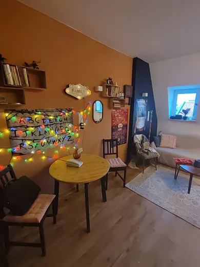 Salon z żółto-pomarańczową ścianą, drewnianym stołem i girlandami.