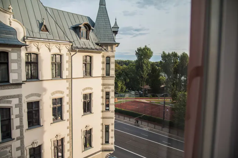 Jasna sofa przy oknie z zasłonami i drewnianą podłogą.