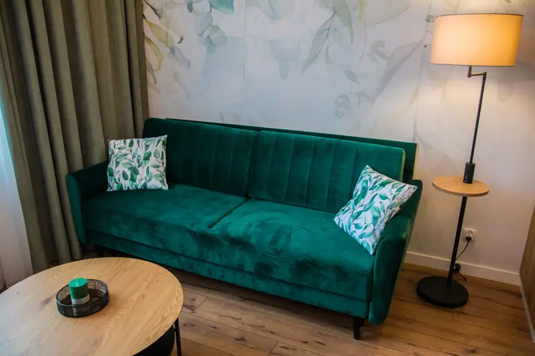 Teal sofa w części wypoczynkowej z lampą stojącą i dekoracyjną tapetą w tle