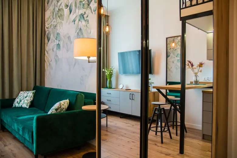 Salon z zieloną sofą, dużym oknem i drewnianą podłogą.