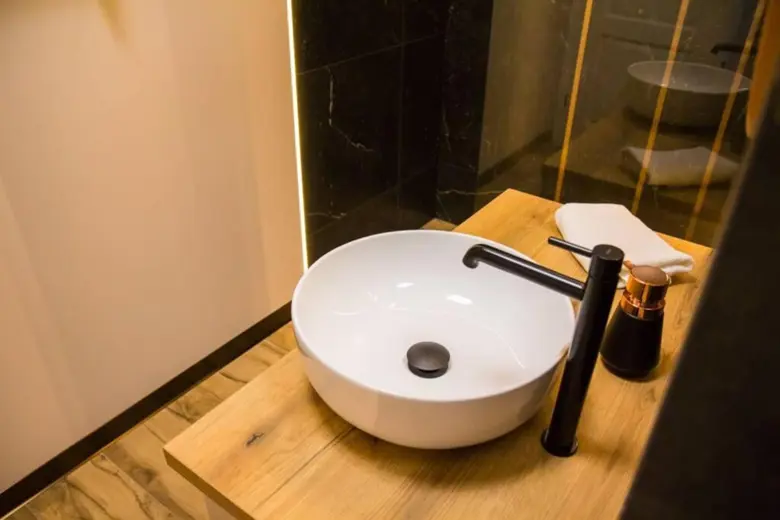 Okrągła miska na drewnianym blacie, czarna armatura i minimalistyczny design