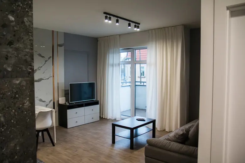 Salon z sofą, dużymi oknami i wyjściem na balkon