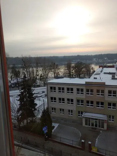 Widok z okna na miasto, rzekę i zachodzące światło.