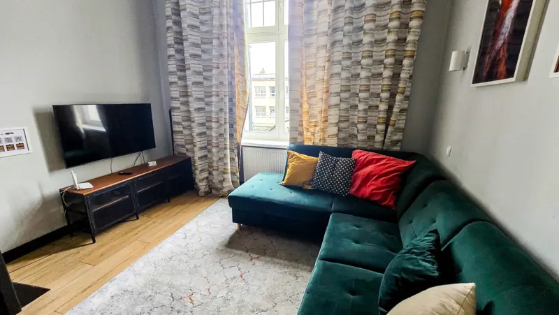Zielona sofa w salonie obok okna i zasłon