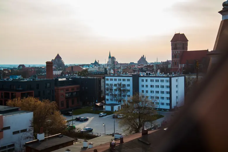 Widok na miasto z dachami, wieżami i zachodzącym słońcem.